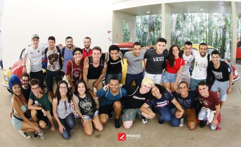 Foto de 23 jovens, alguns de pé e outros ajoelhados em um saguão do Instituto Inhotim. Eles posam para a foto e sorriem.
