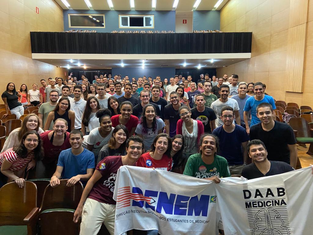 Foto de um grupo de mais de cem pessoas no Salão Nobre da Faculdade de Medicina com uma faixa da DENEM e outra do DAAB na frente
