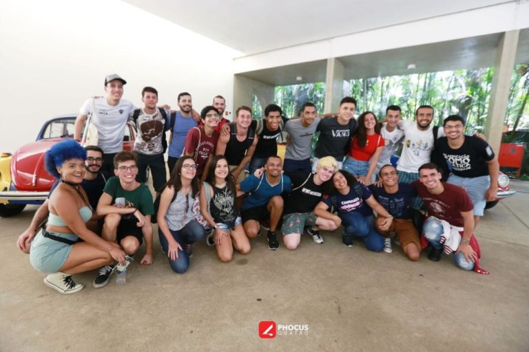 Foto de 23 jovens, alguns de pé e outros ajoelhados em um saguão do Instituto Inhotim. Eles posam para a foto e sorriem.