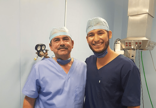 Foto de 2 pessoas abraçadas sorrindo usando roupa cirurgica e touca