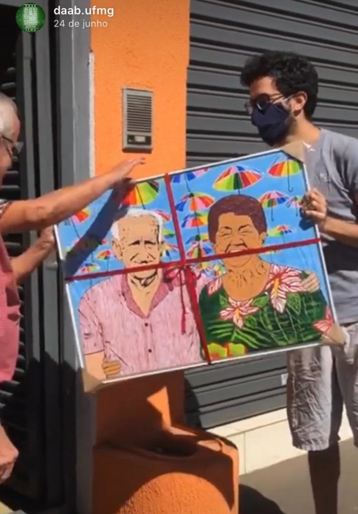 Foto de um rapaz de mascara entregando um quadro pintado para os seus avós