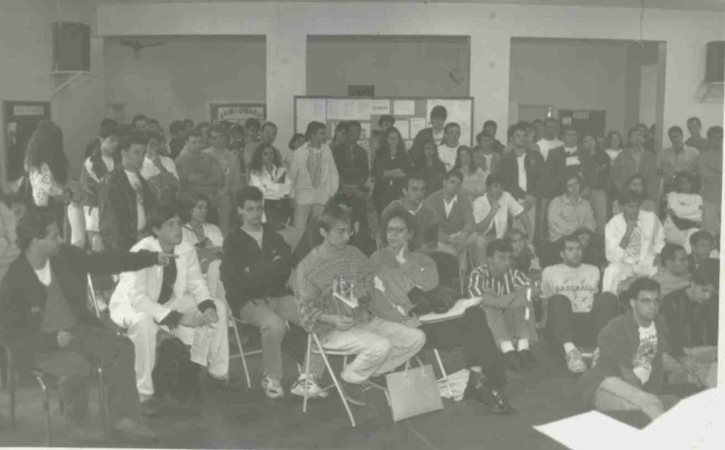 Foto em preto e branco de diversos estudantes sentados olhando todos para uma direção no salão interno do DAAB