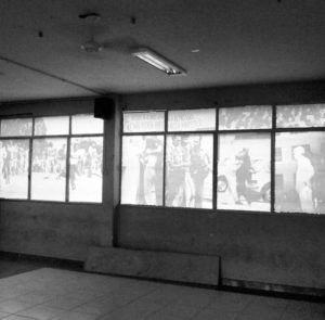 Foto que mostra a janela do salão interno do DAAB que é plotada com fotos da repressão que os estudantes sofreram durante o 3º Encontro Nacional dos Estudantes que foi sediado no DAAB. Na imagem é possível identificar estudantes correndo da opressão militar.