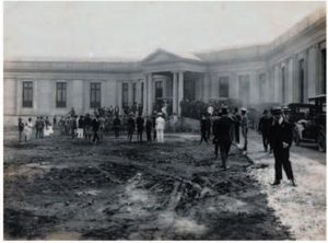 Fotografia em preto e branco do (hoje) ambulatório Borges da Costa, de 1922. A fotografia foi tirada de forma oblíqua do canto esquerdo da face anterior do prédio. Além do prédio, observa-se muitas pessoas, que aparentam ir em direção a entrada do prédio.
