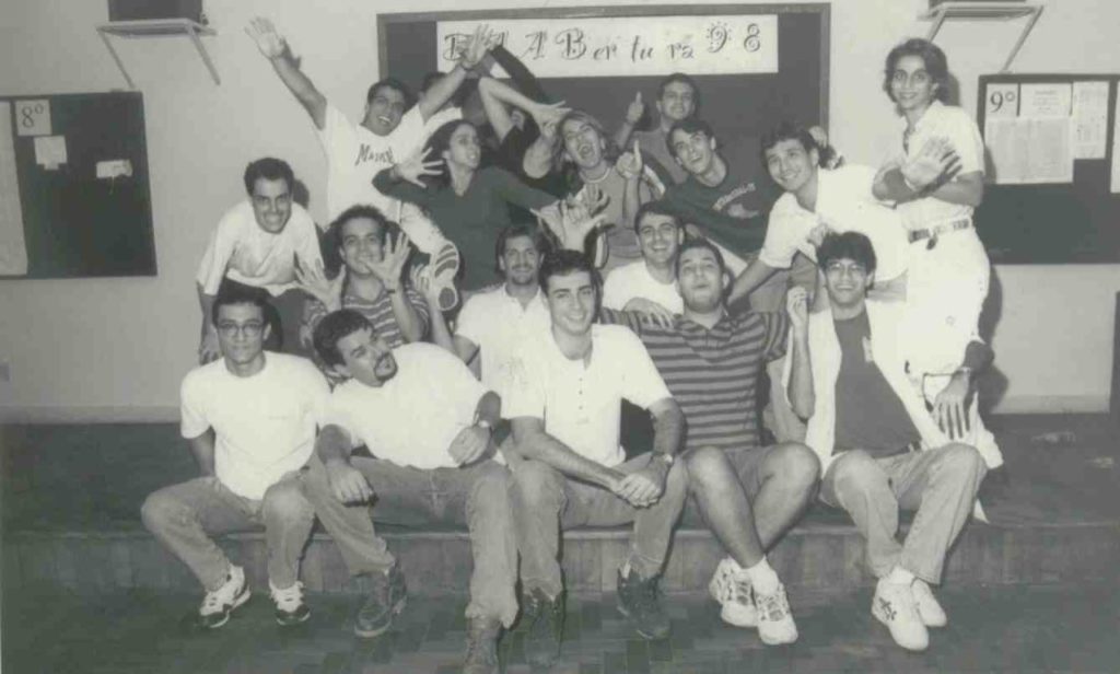Foto em preto e branco, na foto estudantes abraçados sentados no palco do DAAB